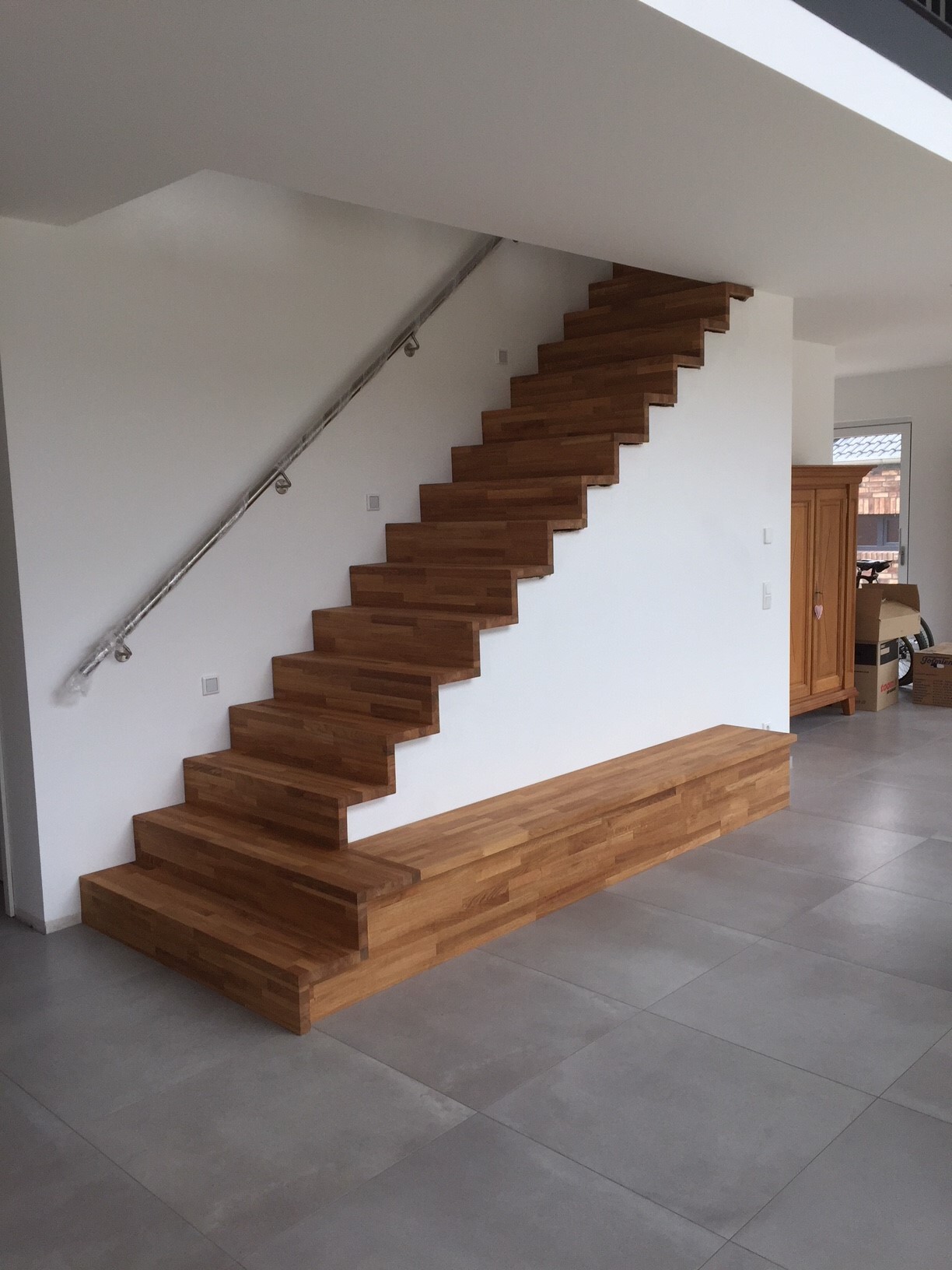 Modern open wooden staircase with metal handrail, underneath a long wooden bench in the living room.