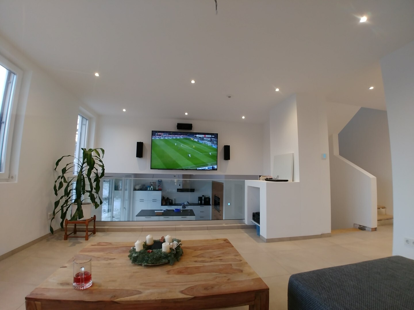 Modern open living area with TV, glass railing, kitchen area below; plant.