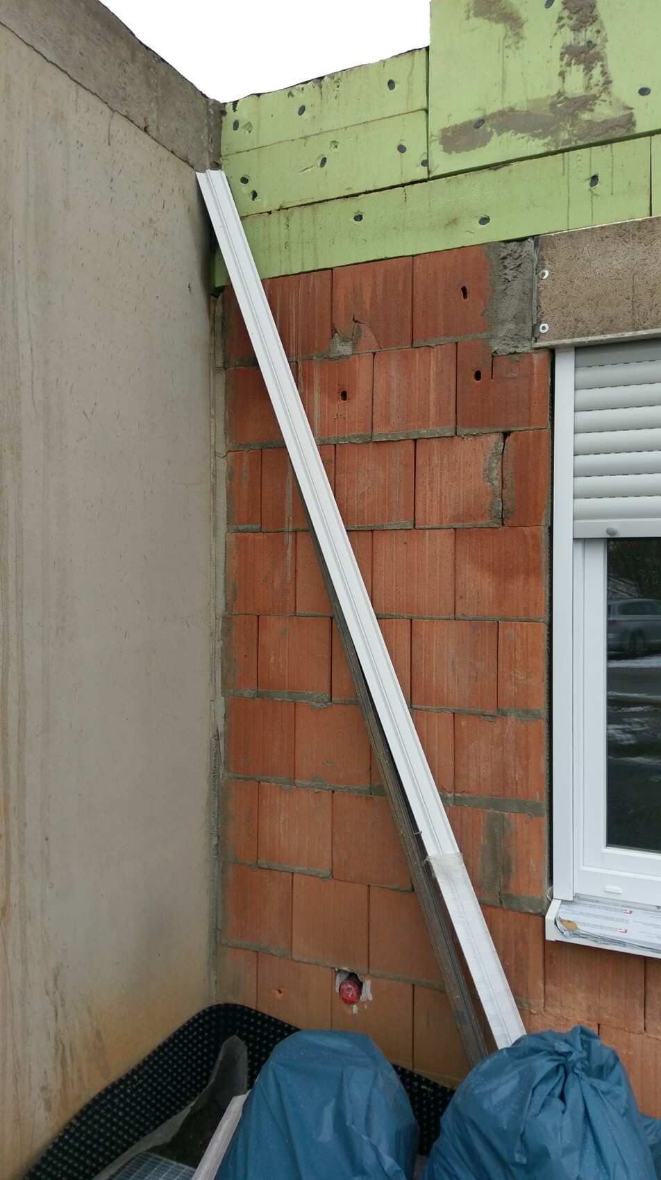 Exterior wall construction with brick, green insulation panels, and window on site