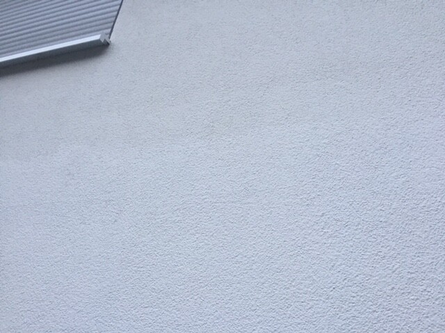 White rough exterior wall with texture and small roof overhang in the upper left area