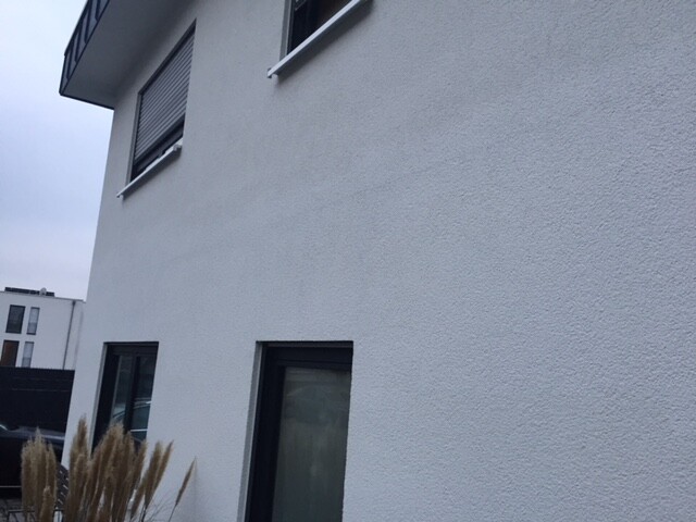 Exterior view of a modern white building with windows and roller shutters