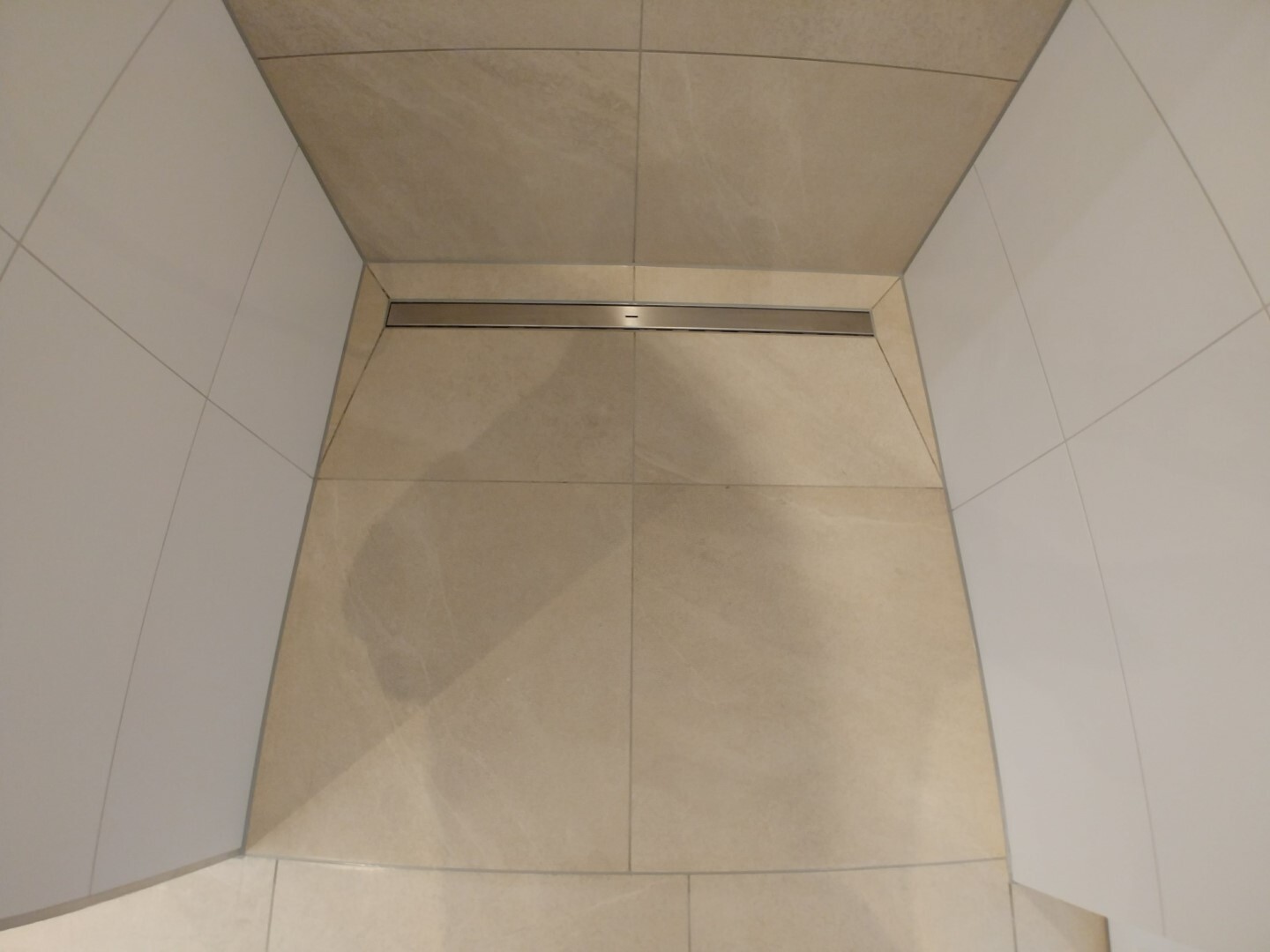 Modern shower with beige tiles, linear metal drain in the floor.