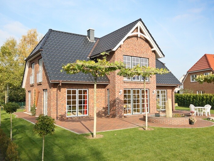 Zweistöckiges rotes Backsteinhaus mit dunklem Dach, großzügigem Garten und Terrasse.