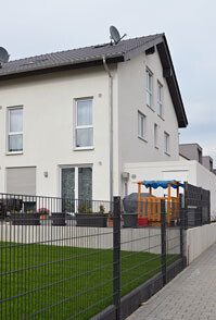 Exterior view of a modern residential house with garden fence and playground equipment