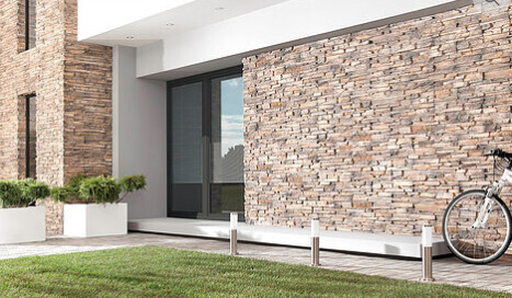 Modern house front with stone cladding, glass entrance door, and green front yard