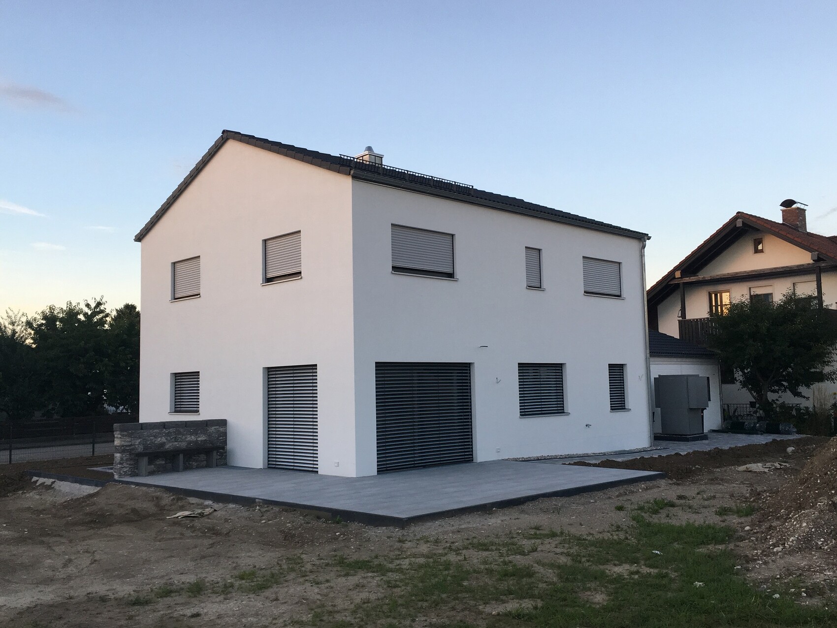 White, two-story house with roller-shutter windows, large garage and paved terrace.