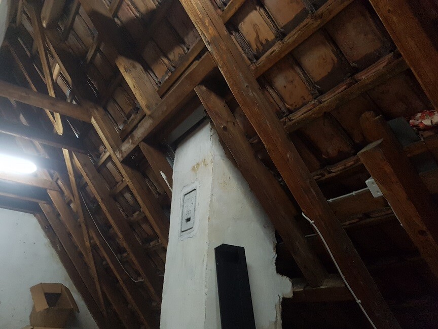 Attic with visible wooden beams, a central white chimney wall, and little light.