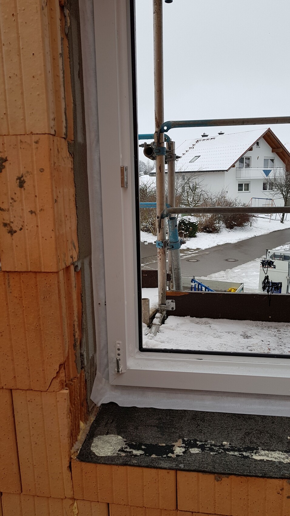 Window frame on a winter construction site with scaffolding and snow cover.