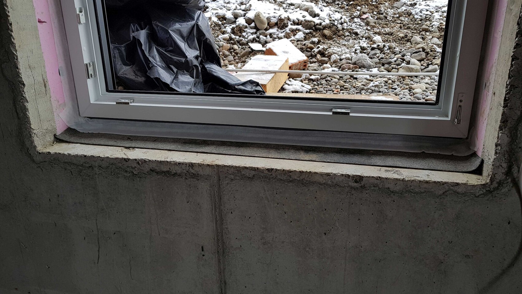 Window in shell construction in concrete wall, outside with construction debris and gravel.