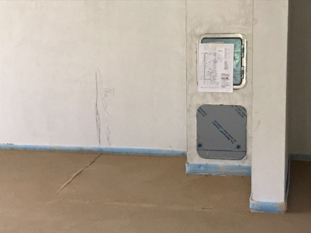 Unfinished interior construction site: white walls, blue floor covering, installation opening in wall.