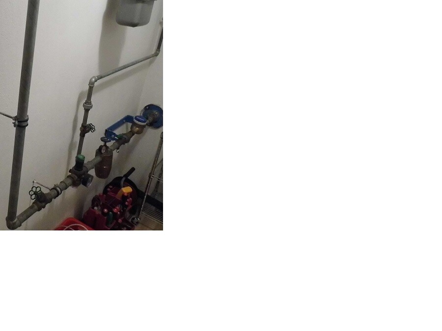 Wall with metal pipes, valves, and fittings in a sanitary room.