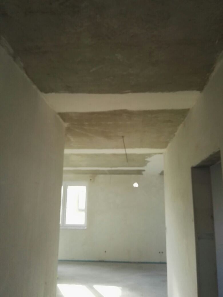 Unfinished interior of a shell construction with concrete ceiling, unplastered walls, and window.