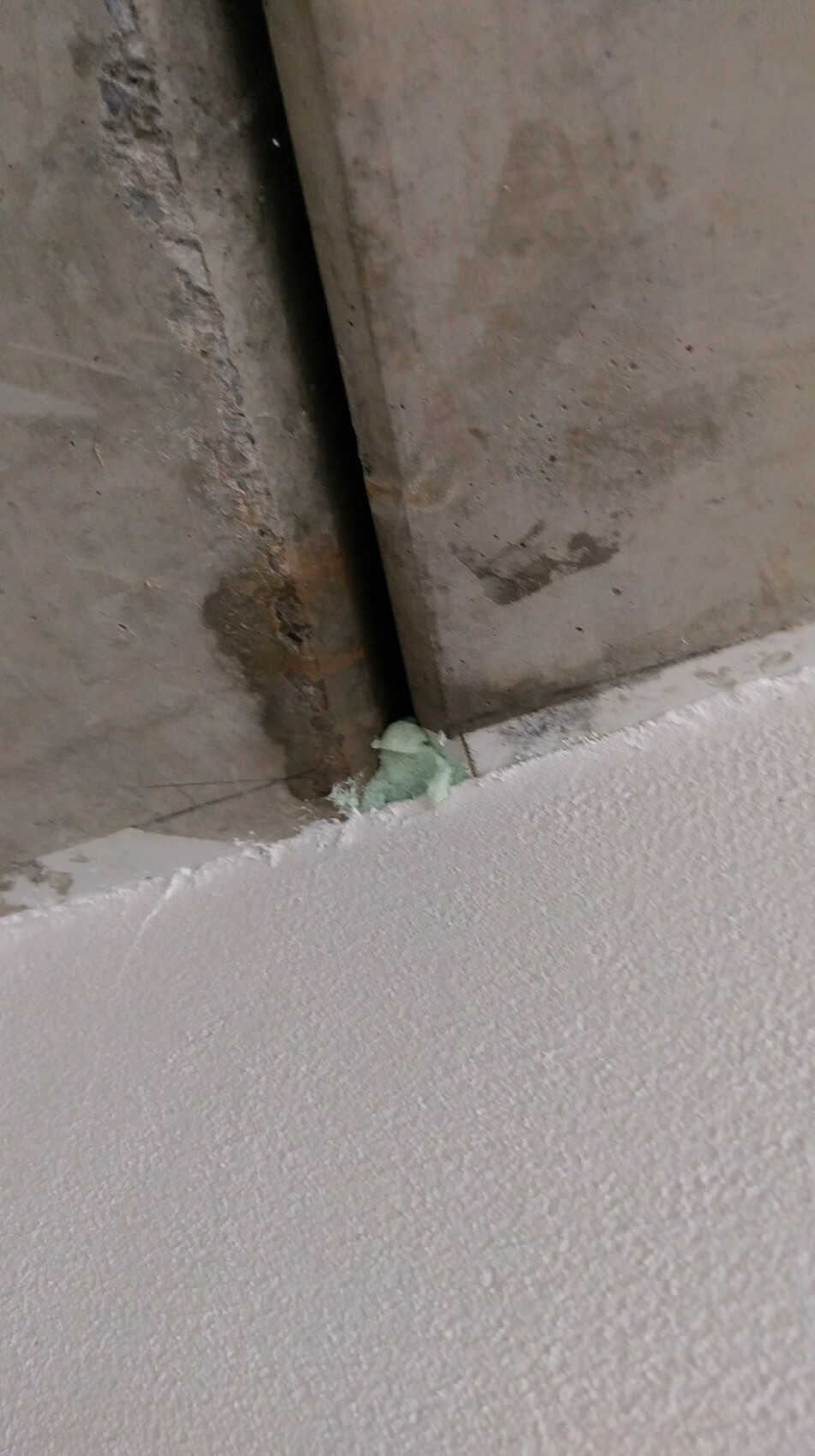 Rostige Metallkante zwischen Betonwand und Boden mit grünem Dichtmaterial