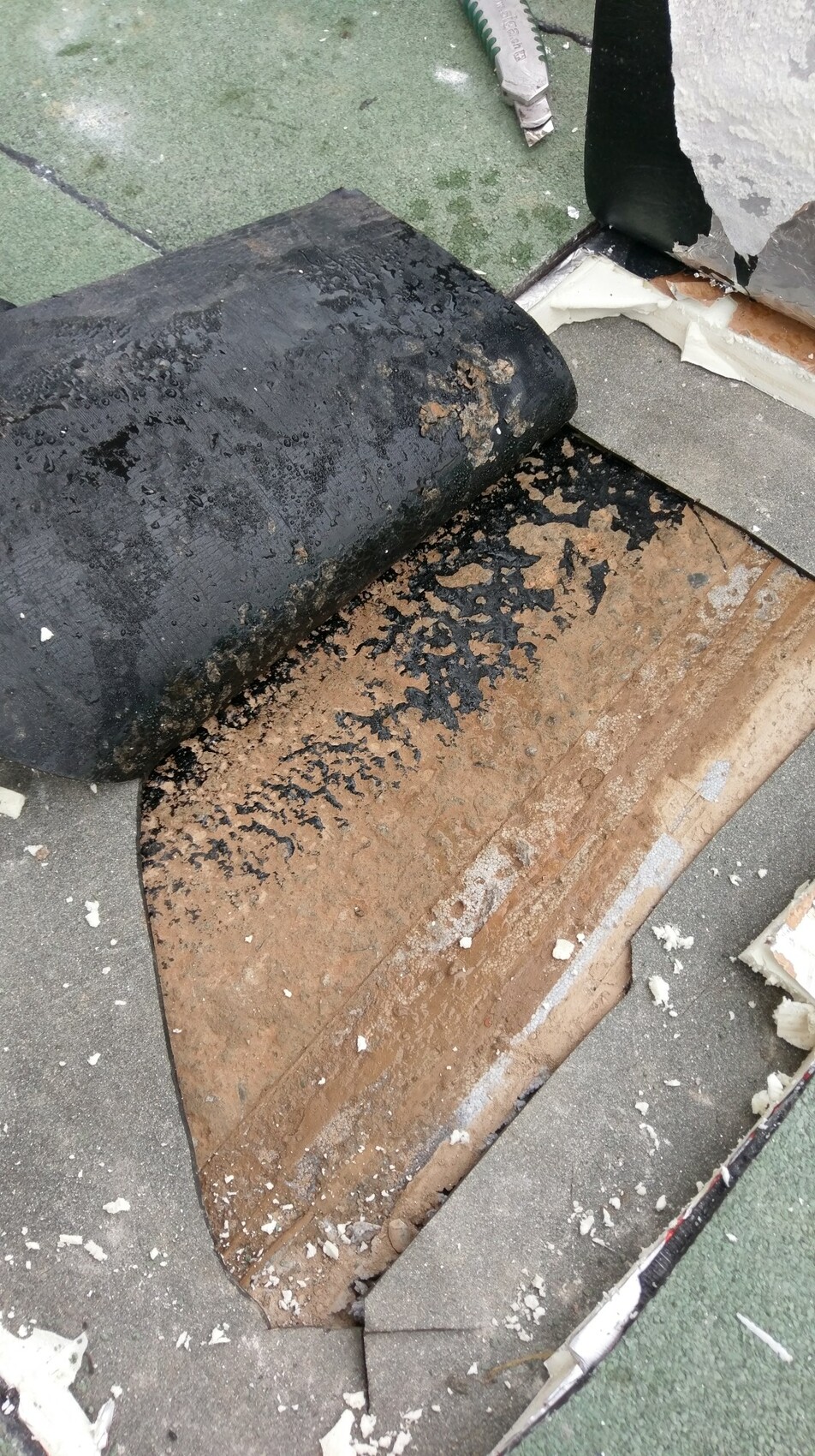Baustelle mit aufgelegter schwarzer Dichtungsbahn auf braunem Untergrund und Bauresten.