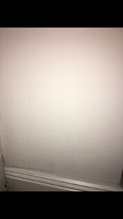 A white interior wall with skirting board and light stains in the lower corner.