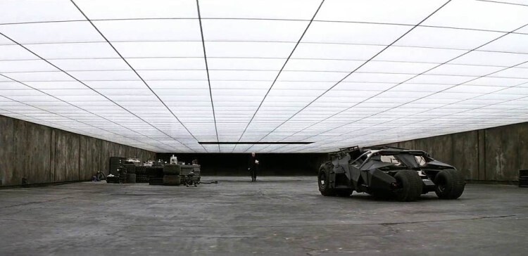 Large dark interior hall with bright ceiling panels, an open vehicle on the right, pallets on the left.