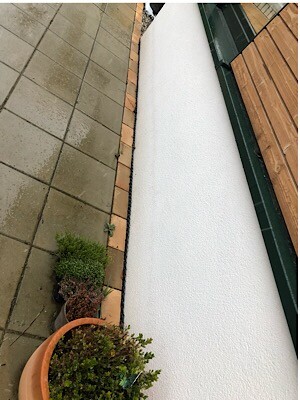 View of terrace with gray tiles, white wall, and wood cladding; potted plant in the foreground.
