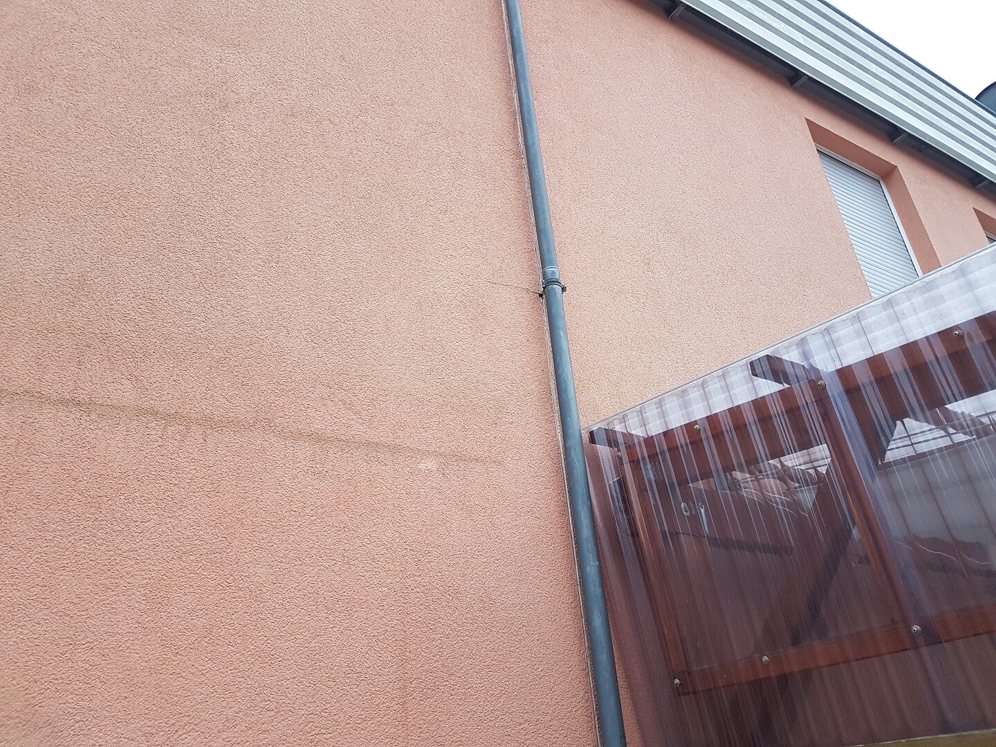 Exterior wall in peach-colored texture, rain gutter, window with roller shutter and balcony roof.