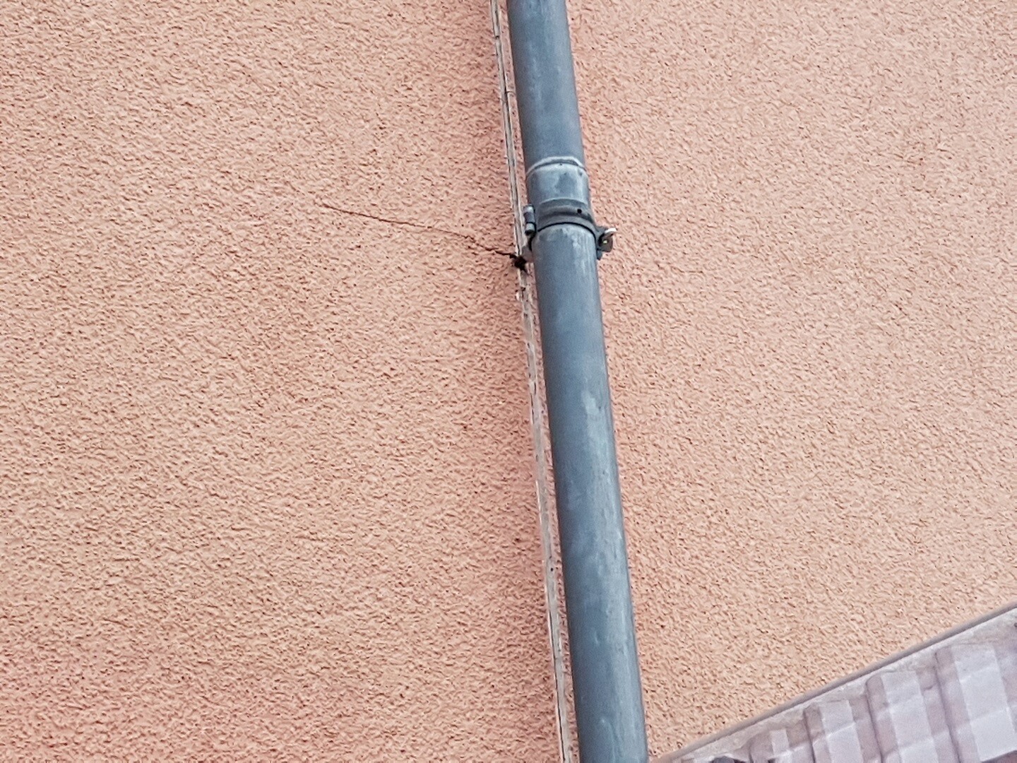 Gray external pipe on orange-painted house wall, part of building services.