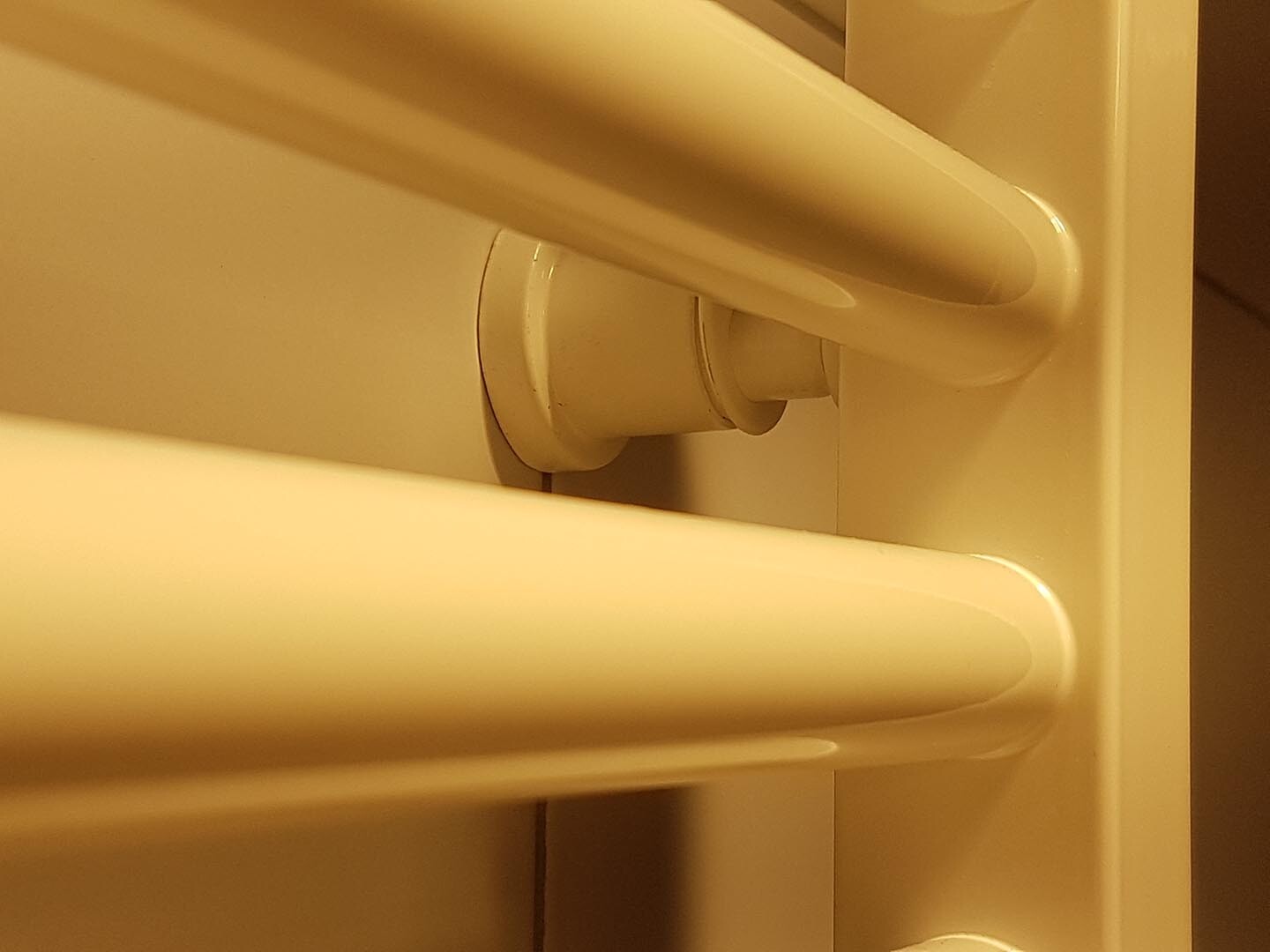 Close-up of a white towel radiator with horizontal pipes under warm indoor lighting