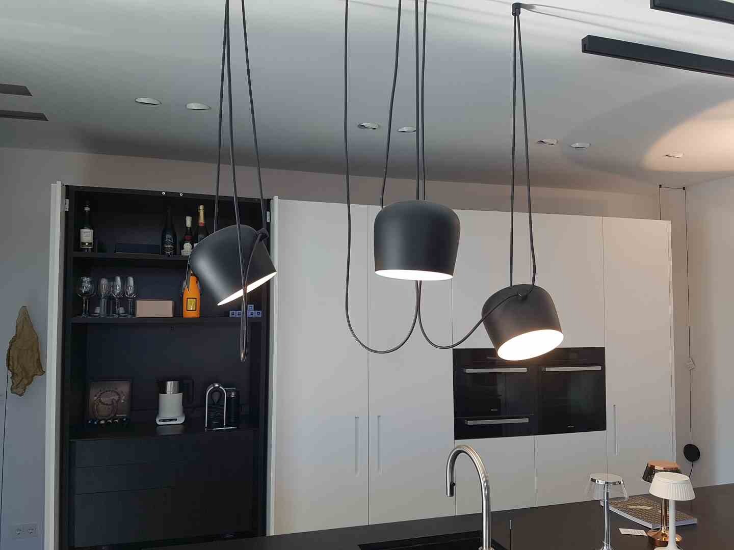 Moderne Küche mit weißen Schränken, Insel und drei schwarzen Pendelleuchten über der Arbeitsfläche.