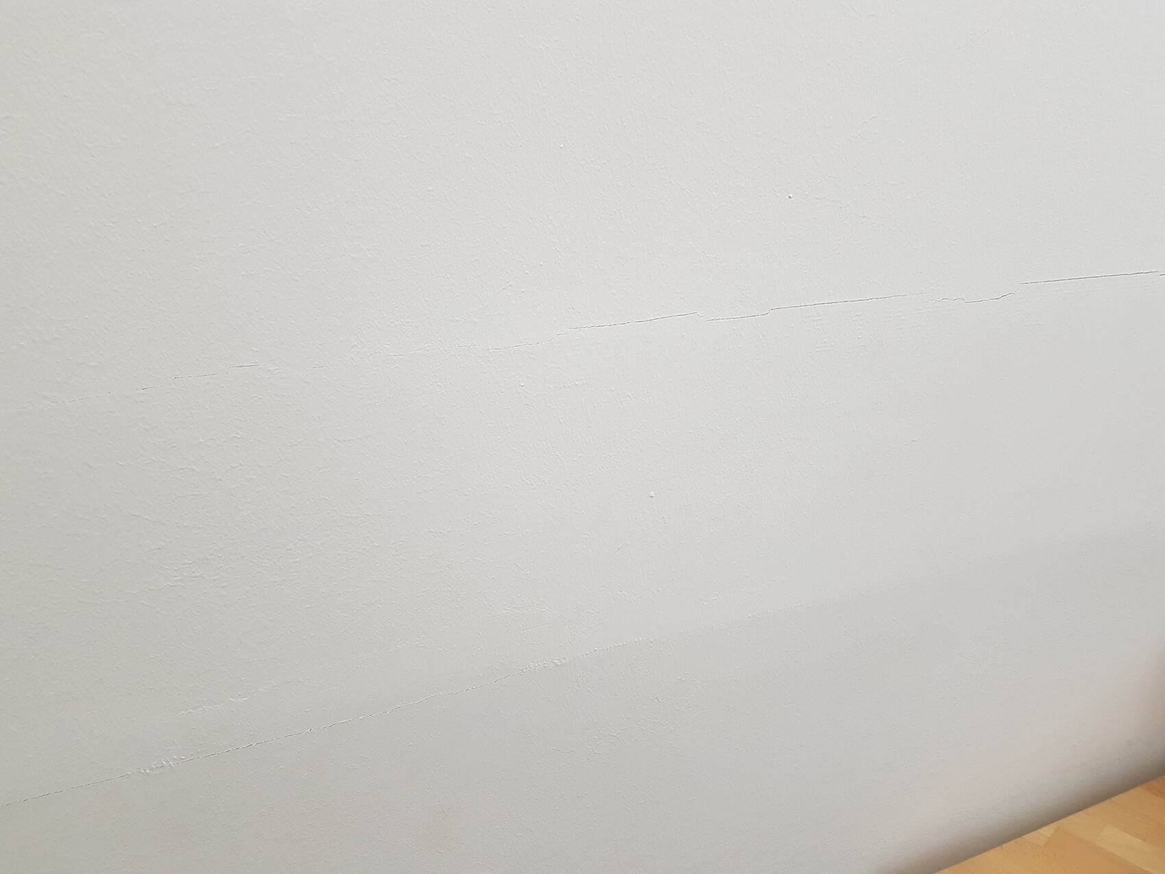 White interior wall with fine cracks, wooden floor visible at the bottom edge