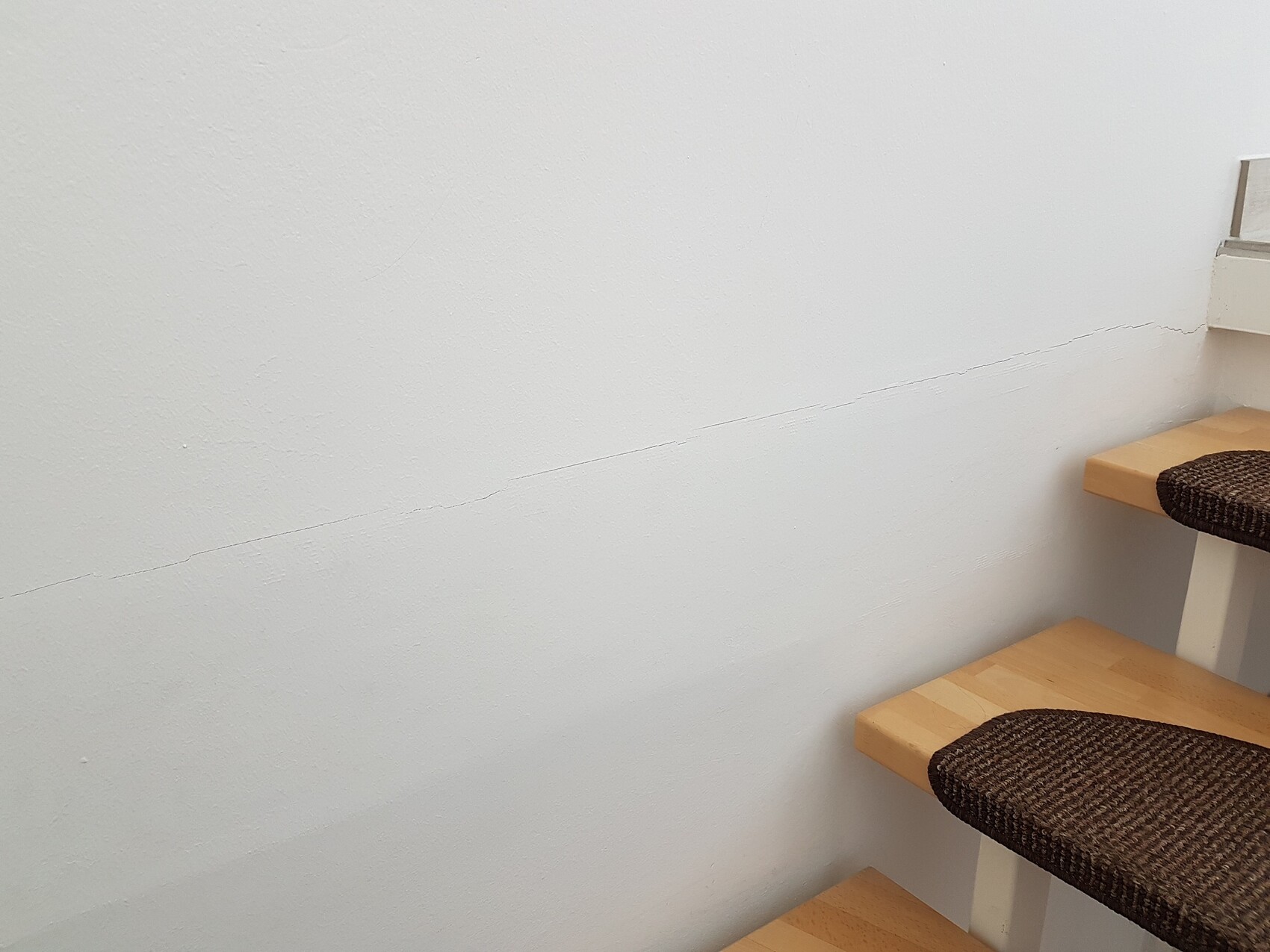 White interior wall with a long diagonal crack next to a staircase with wooden steps.