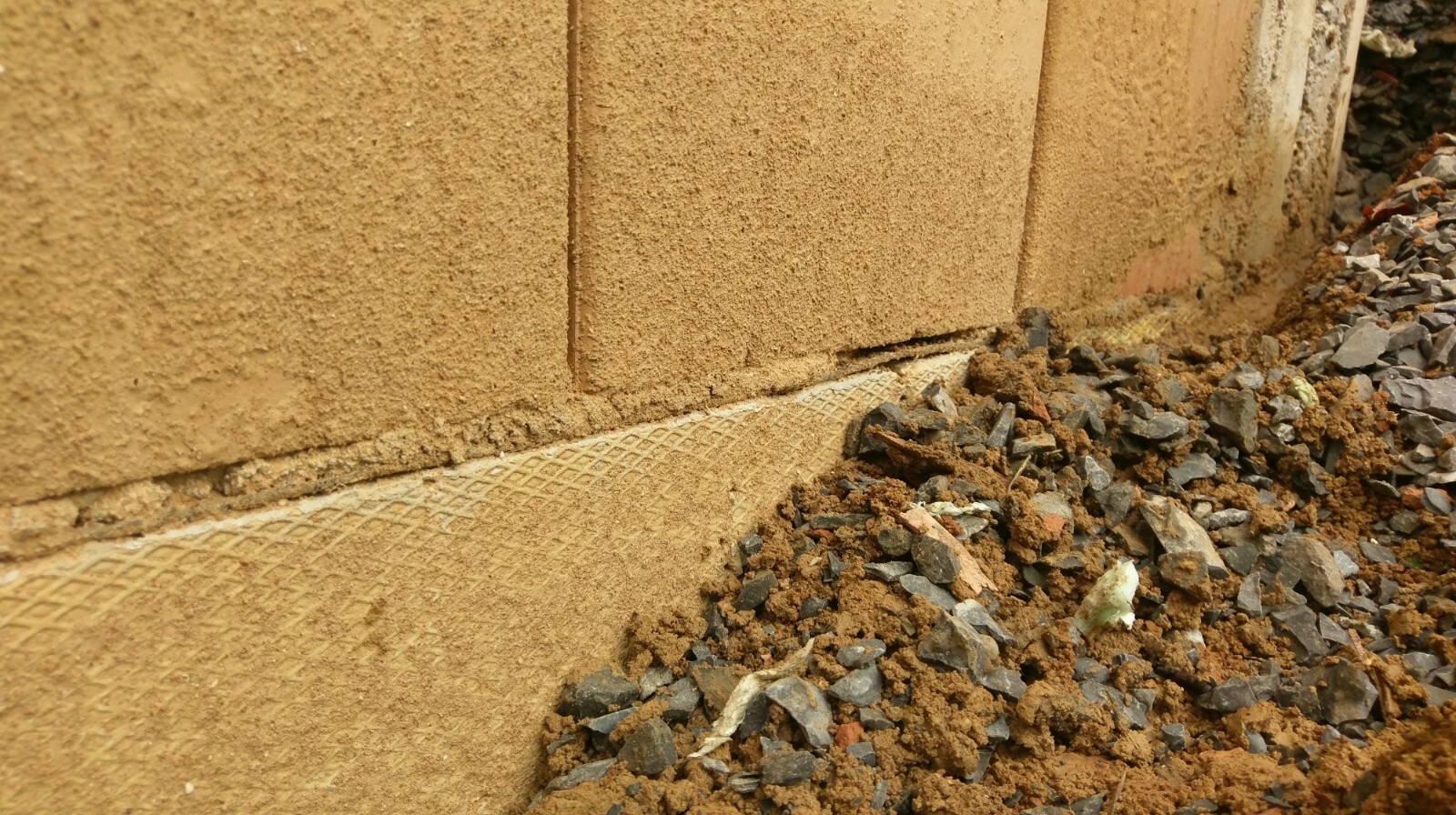 Close-up of a building’s foundation edge with gravel and soil at the construction site.