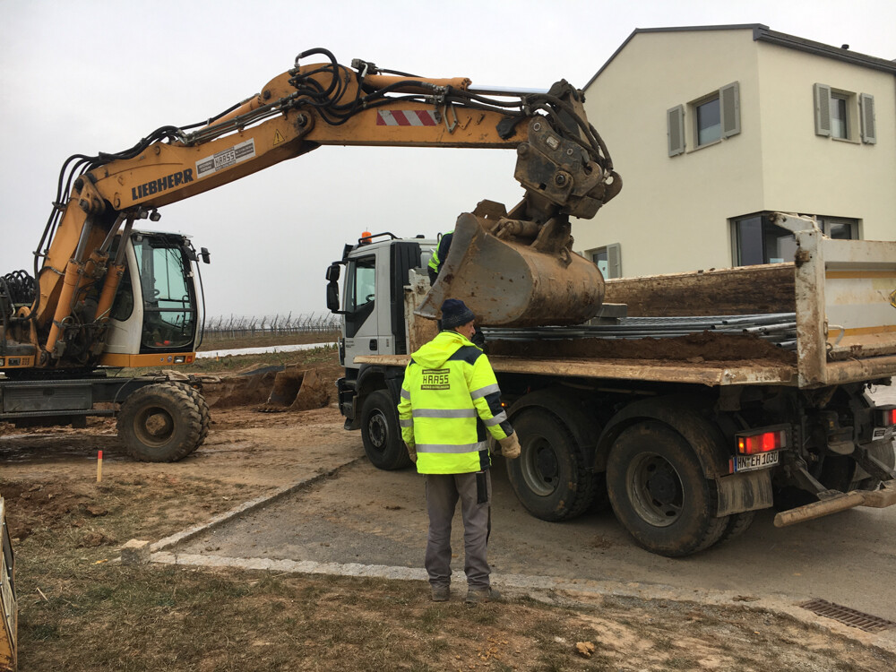 Construction worker in neon vest at site next to large excavator and dumper in front of residential house