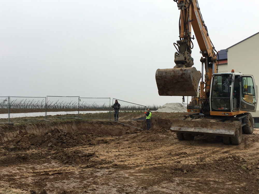 Large excavator digging at construction site, two workers in the background