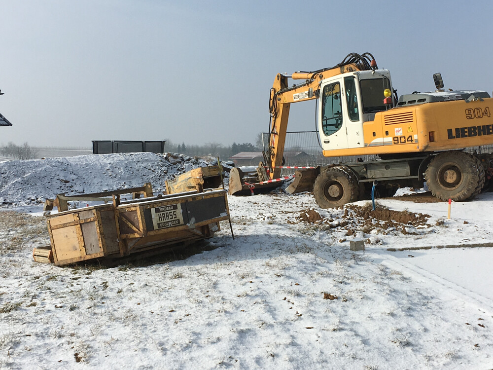 Snow-covered construction site with yellow excavator and construction trailer