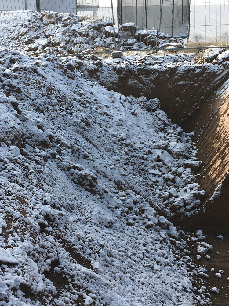 Snowy construction pit with excavated earth behind fence