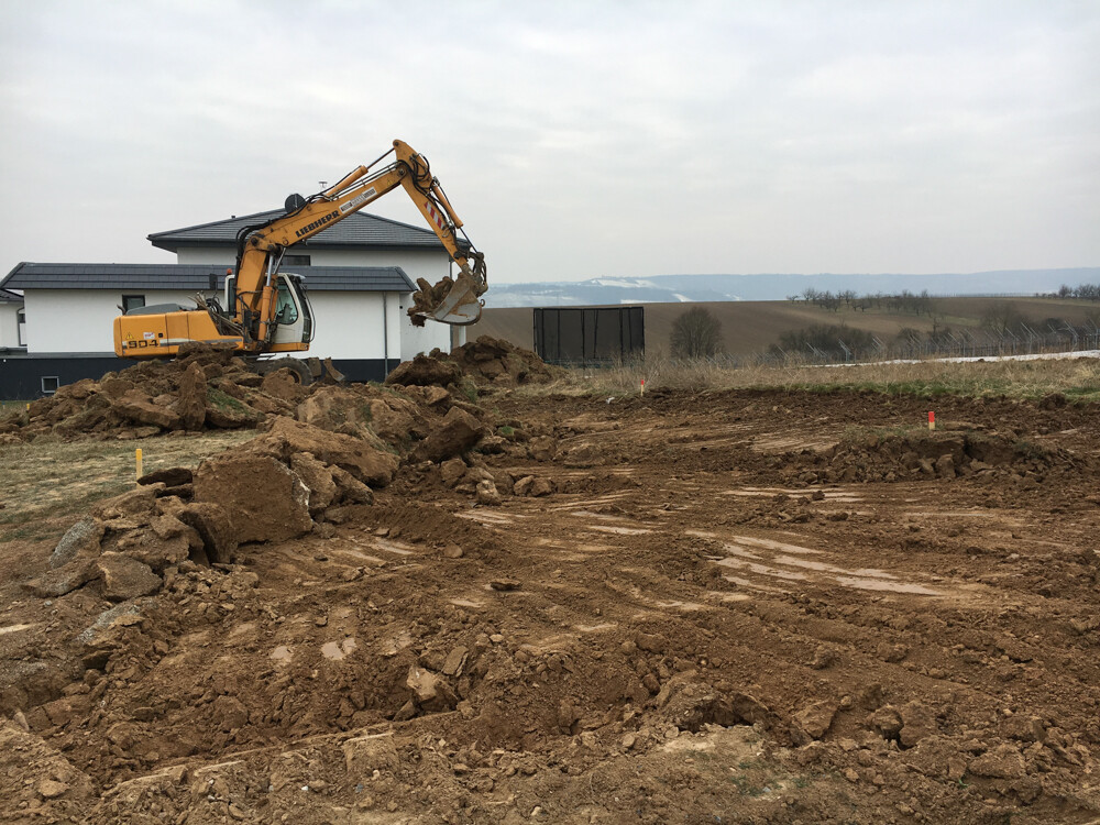 Excavator digging earth at a construction site in front of a single-family house – shell construction and foundation work