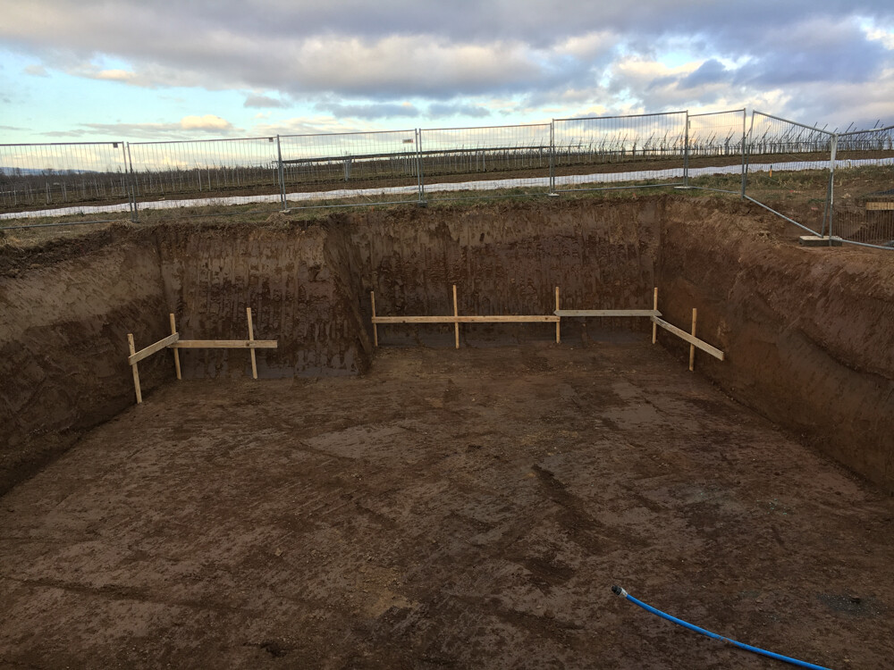 Open excavation supported by wooden beams for foundation work at construction site behind fence