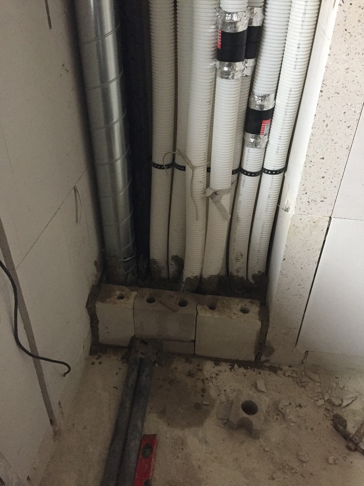 Several white ducts standing vertically next to a concrete foundation; construction materials on the floor.