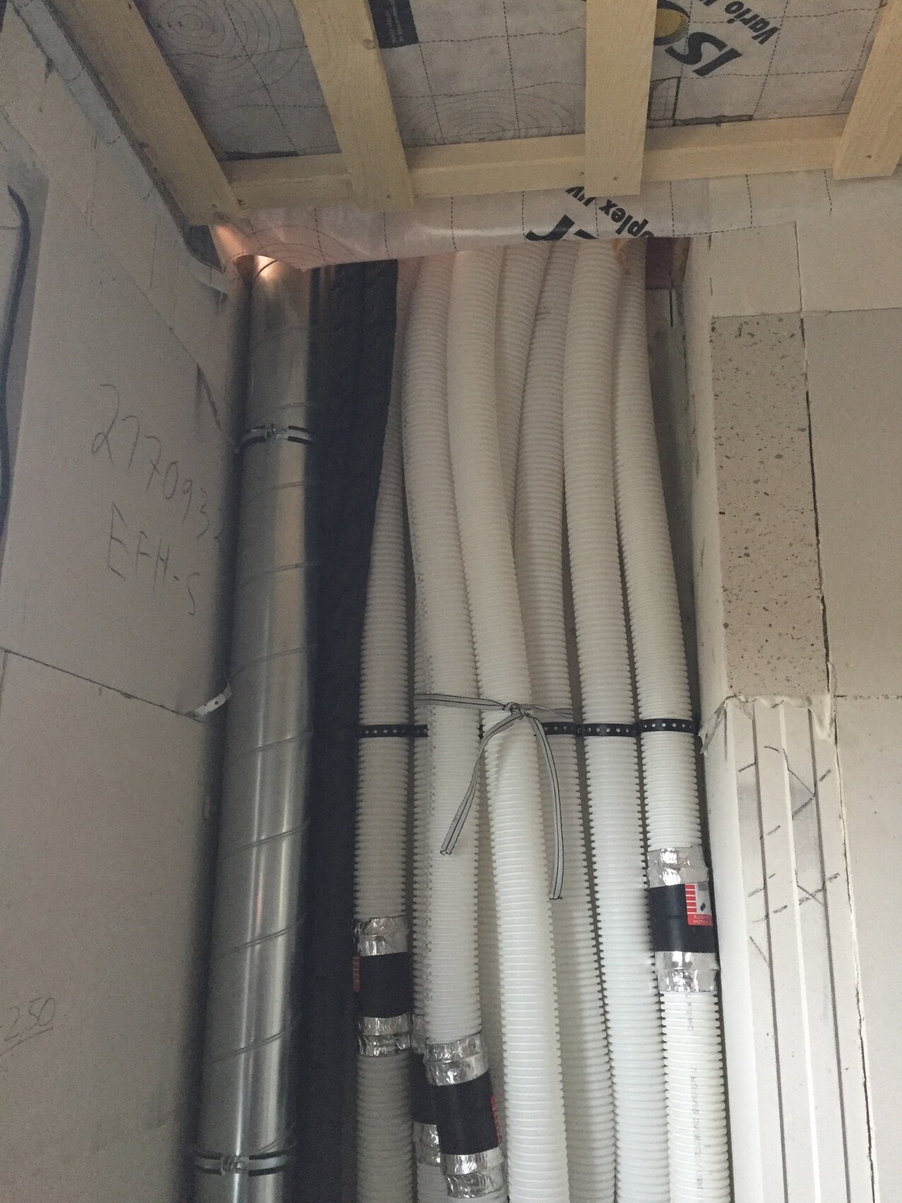 White bundled flexible ducts/ventilation ducts running vertically along the wall; metal duct on the left.