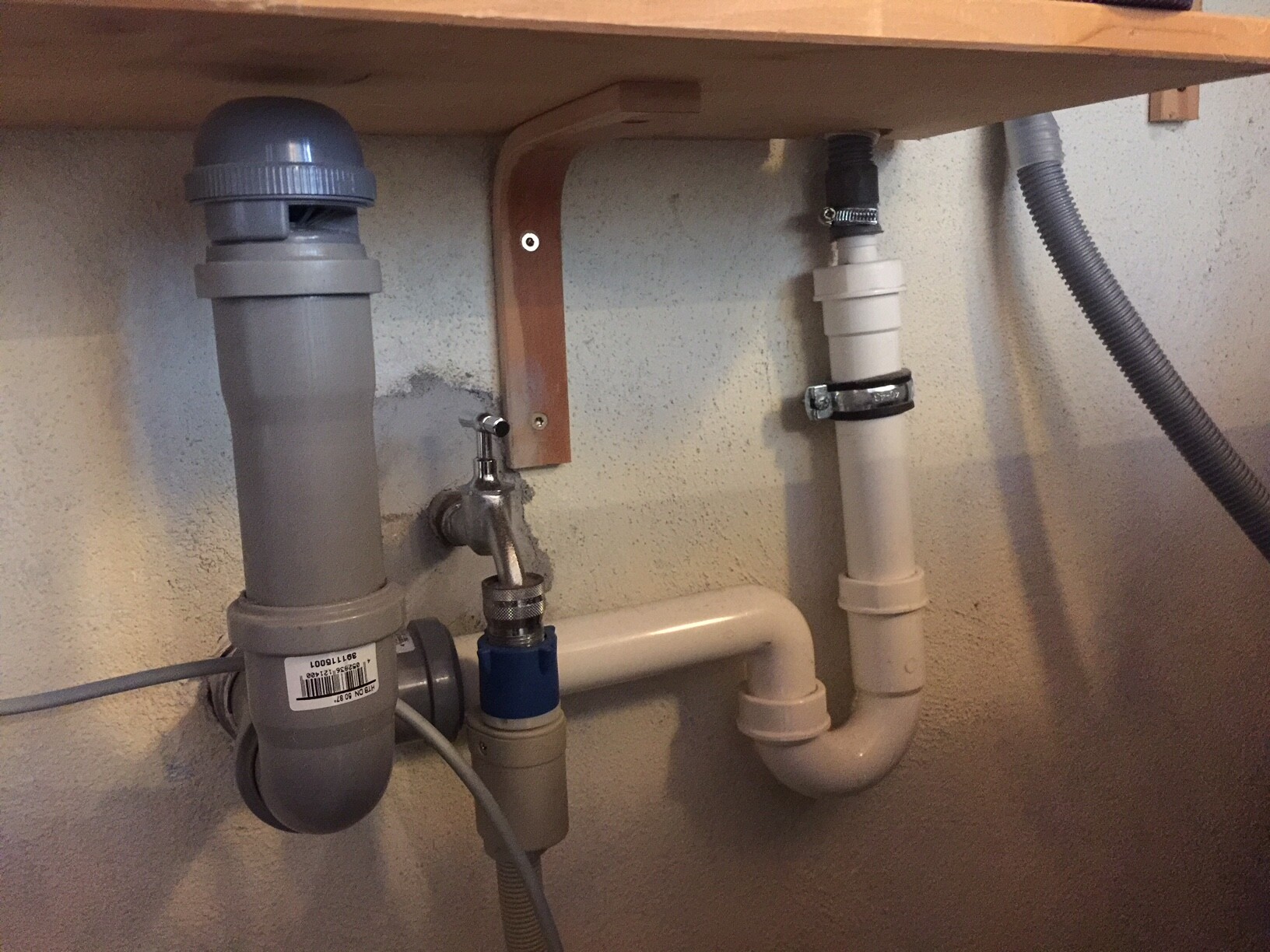 PVC drain pipes visible under the sink, trap, blue shut-off valve, clamps.
