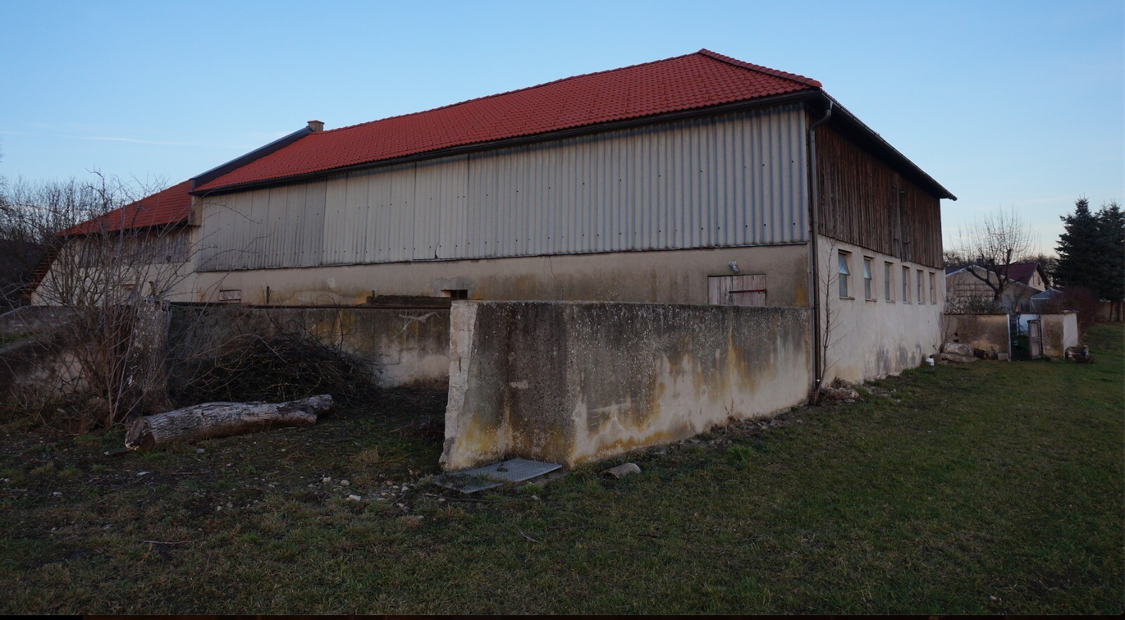 Lange Halle mit rotem Dach, graue Metallverkleidung und Betonfundament, Außenbereich.