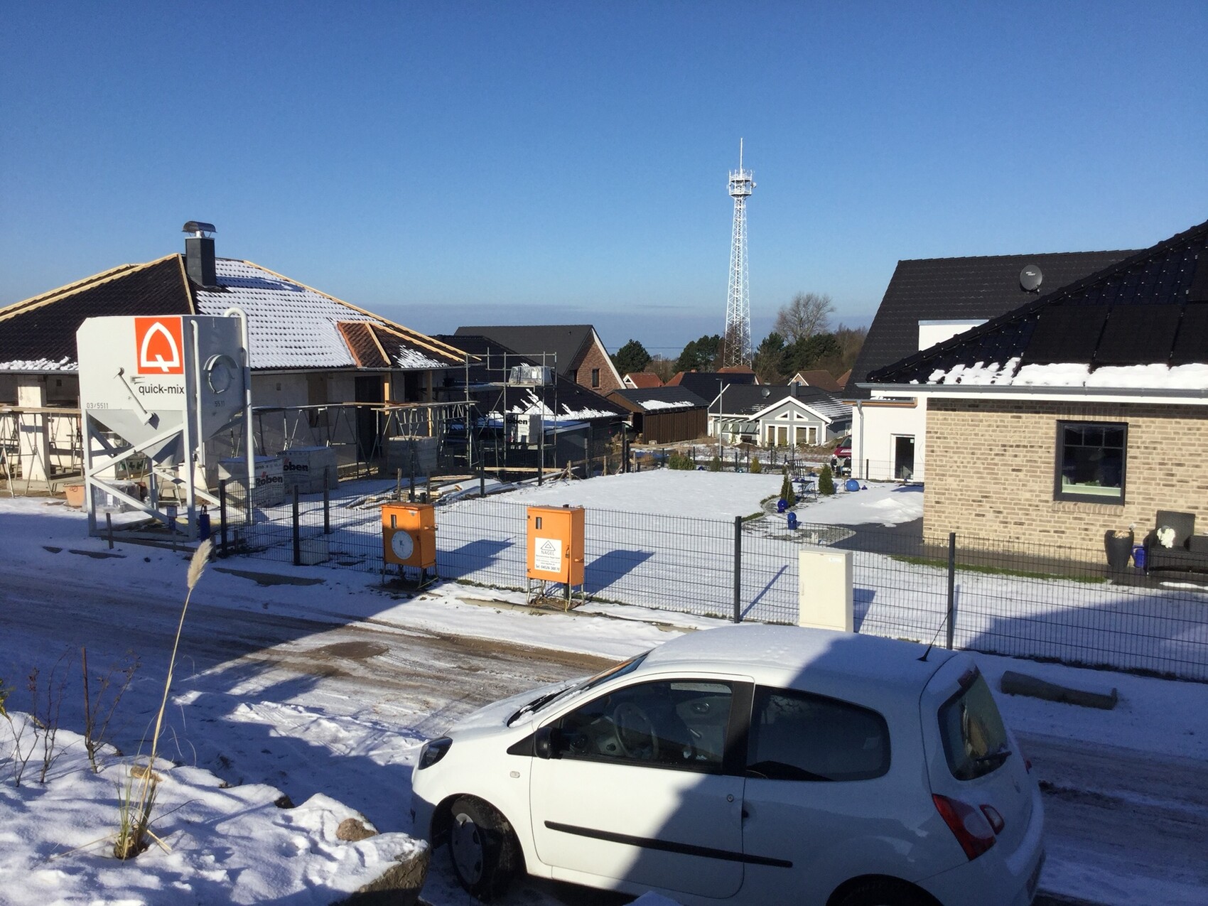 Bauplatz mit Rohbau, Gerüst, Zäunen und Schnee vor Wohnhäusern im Winter