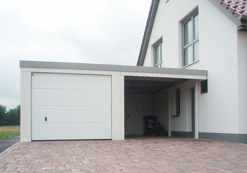 White house front with closed garage on the left, open carport on the right; bicycle in the carport.