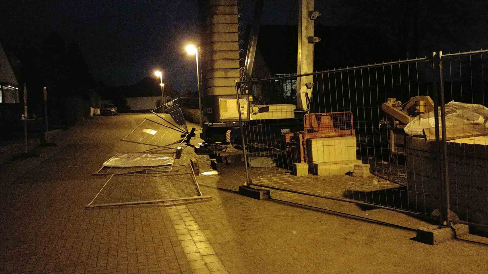 Night view of a construction site by the roadside with fences, metal plates, and crane.