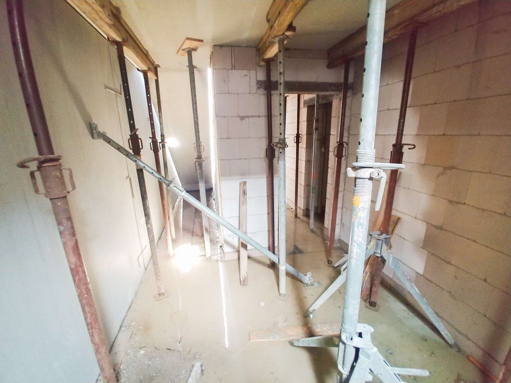 Raw corridor with steel supports, scaffold posts and wet floor.