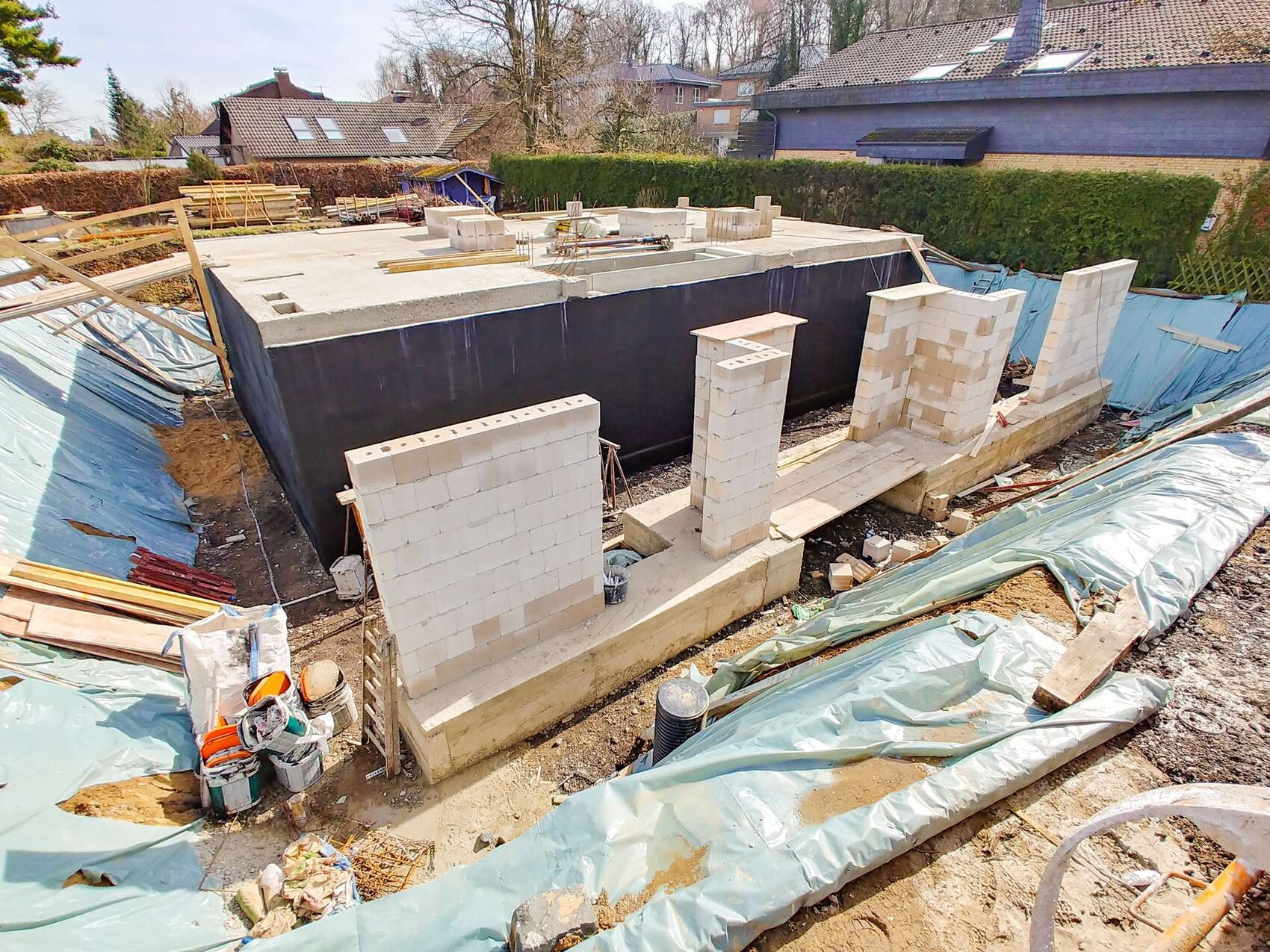 Construction site with foundation walls made of concrete blocks, lumber and tarps around.