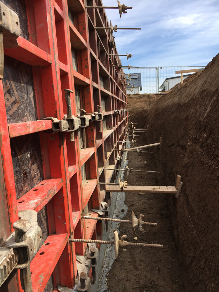 Red steel frame formwork with bolts and supports at an excavation pit.