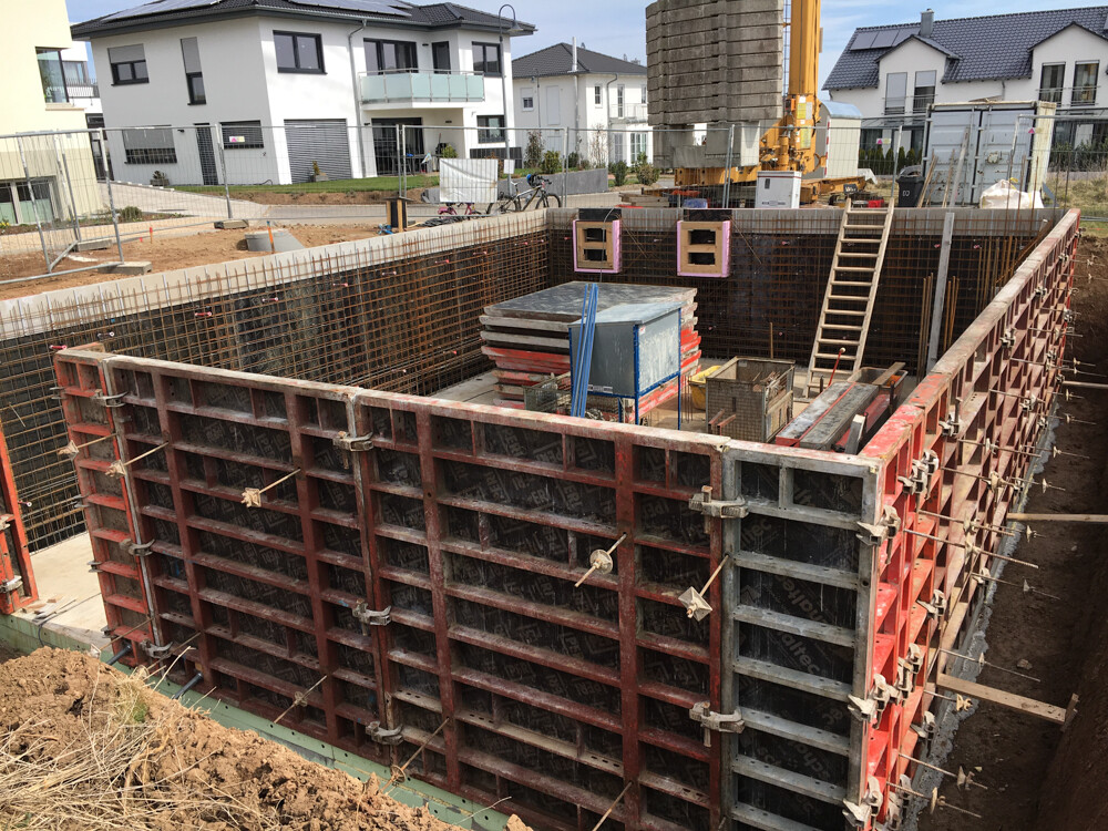 Excavation pit with formwork frame, reinforcement, construction crane; residential houses in the background