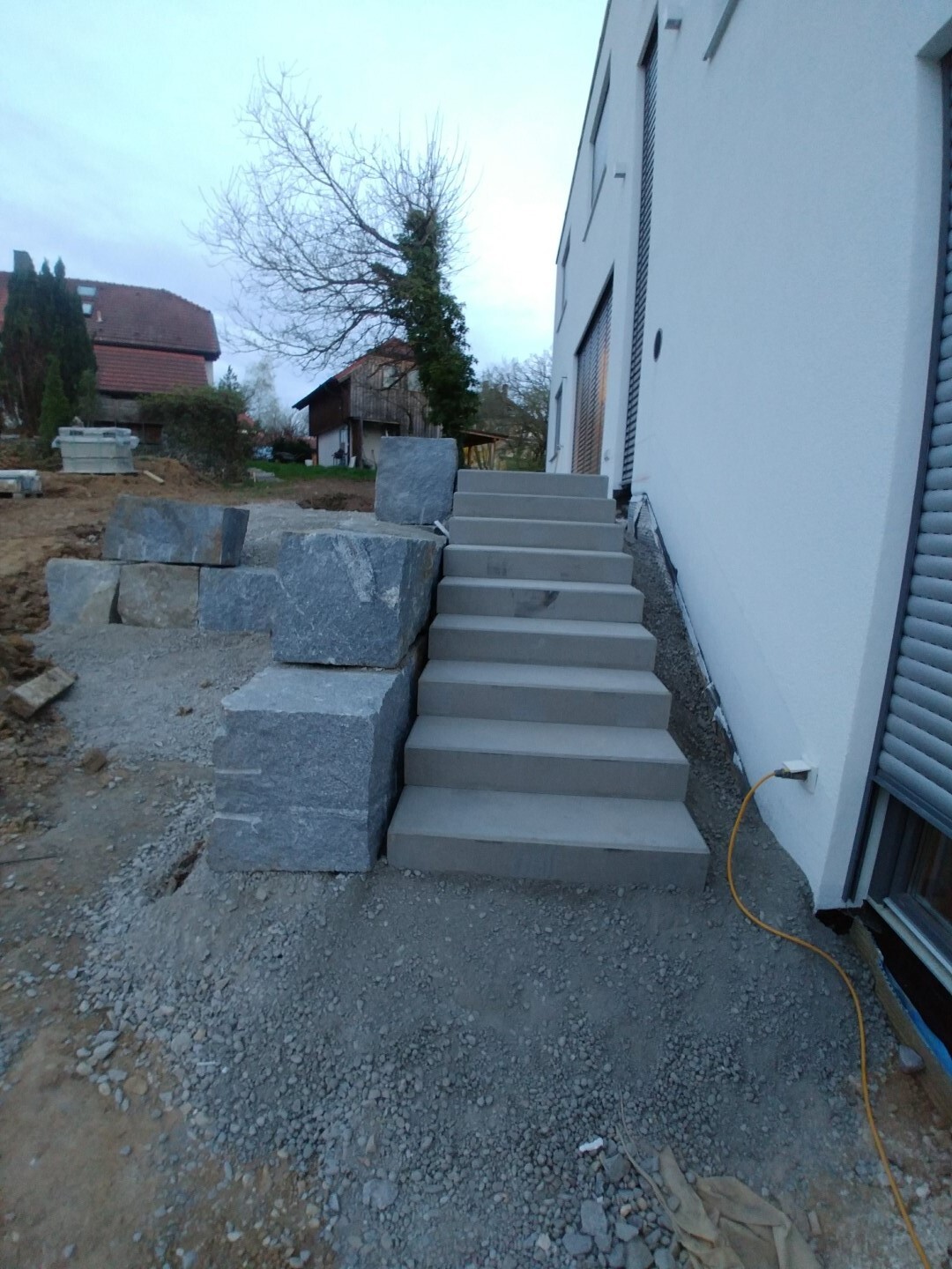 New concrete stairs next to the white house; left stone block retaining wall, gravel subbase