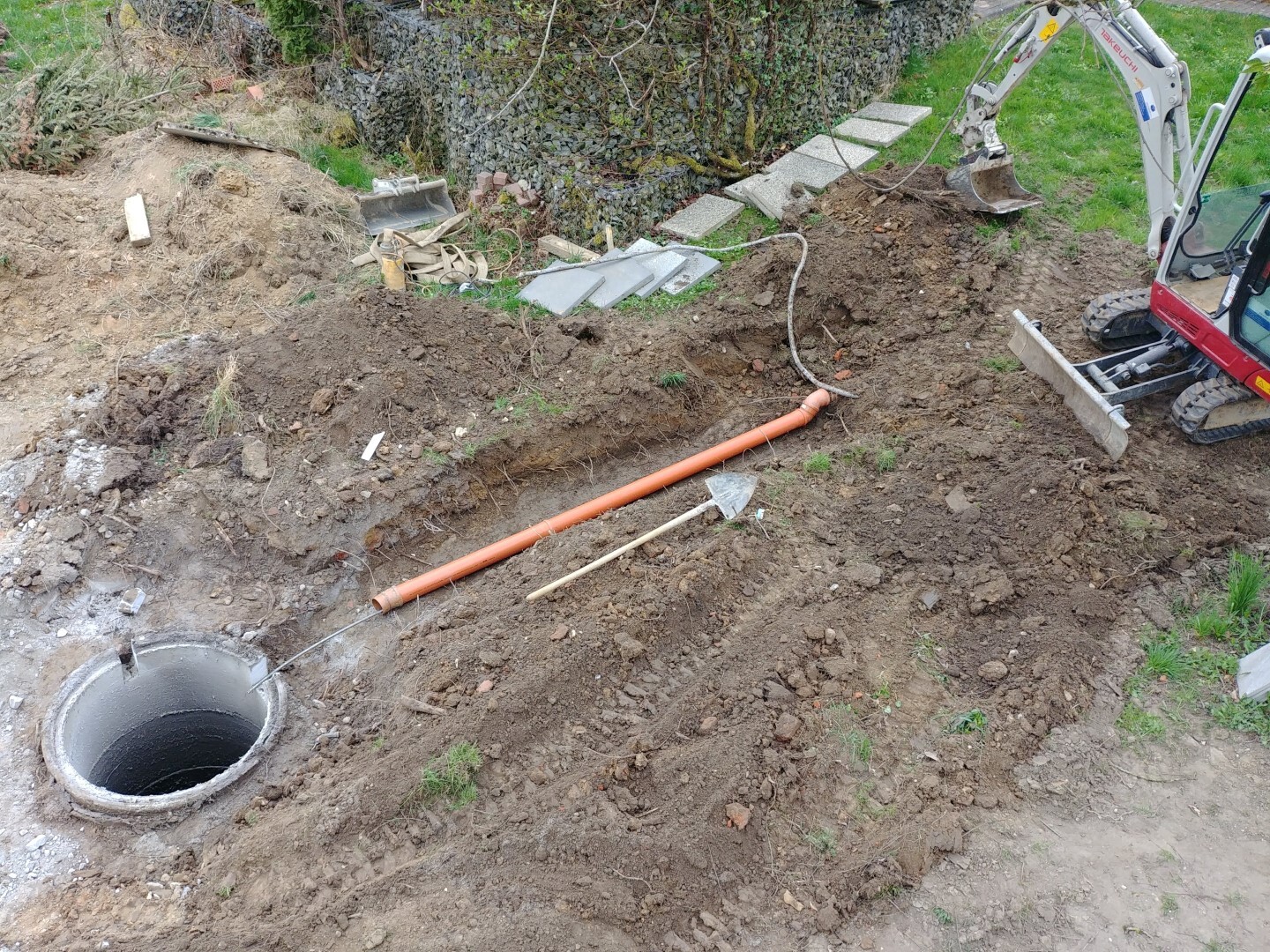Excavation with exposed soil, orange piping and excavator during foundation work