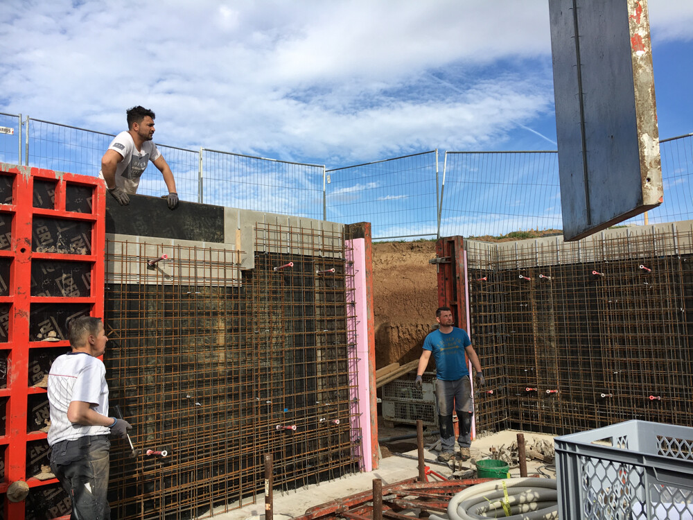 Construction workers working on steel reinforcement and concrete wall at a construction site.