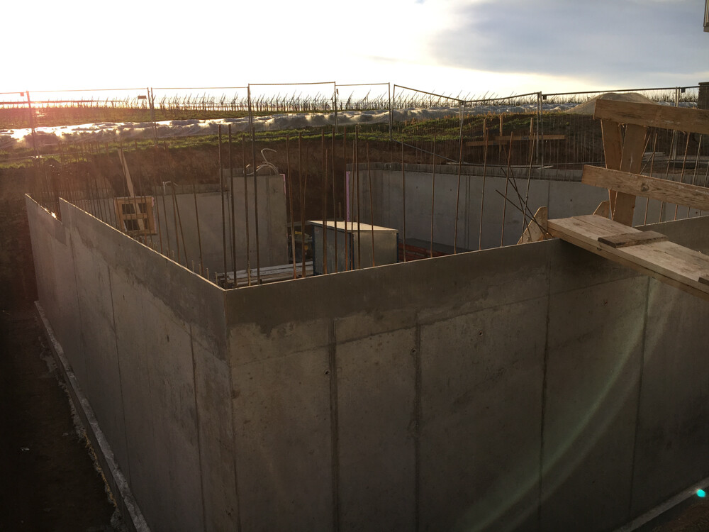 Concrete foundation with steel reinforcement, wooden formwork elements and evening sun over the excavation.
