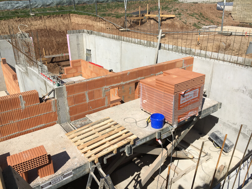 Shell construction site: brick walls being built, pallets of bricks, blue bucket on concrete platform.
